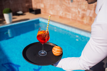 Waiter in white shirt serving red cocktail and orange at pool terrace