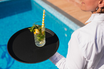 A waitress in a white shirt serves a mojito cocktail to guests by the pool. Crazy summer party...