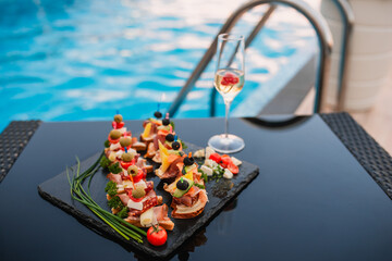 Canapes placed on a tray, while next to the champagne with strawberries by the pool. Summer party at the pool