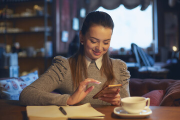 Beautiful woman sitting in a cafe at a table drinking tea and making notes in a notebook