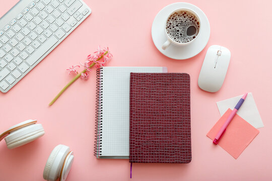 Girly desktop with notepads computer headphones cup of coffee on pink color background. Work office space. Working desk for schoolgirl student or office worker. Home inspirational office desk. Flat