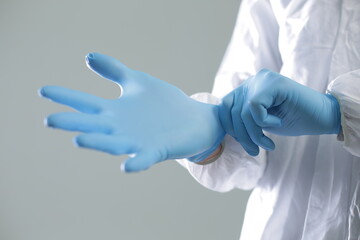 Doctor in a protective medical suit puts on blue rubber gloves