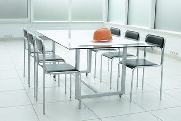 Construction hard hat and blueprints on glass table in office space