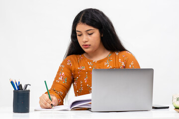 Pretty young Indian woman sitting against white backdrop and using her laptop. Cute teenager doing her online schoolwork from home.