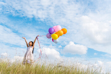 Cheerful cute girl holding balloons running on green meadow white cloud and blue sky with happiness. Hands holding vibrant air balloons play on birthday party happy times summer on sunlight outdoor