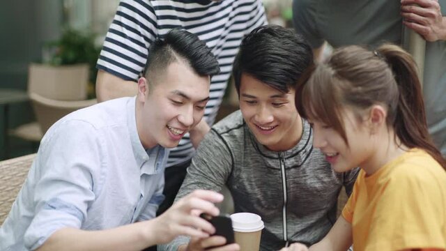 group of young asian adult four men and a woman sitting in outdoor cafe sharing cellphone photo 