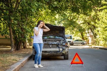 Driver woman in front of wrecked car in car accident. Scared woman in stress holding her head after auto crash calling to auto insurance for help. Dangerous road traffic situation.