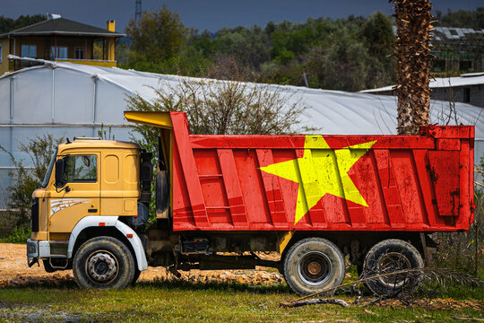 Dump truck with the image of the national flag of Vietnam is parked against the background of the countryside. The concept of export-import, transportation, national delivery of goods