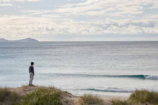 Boy Standing On Sand Dune Looking Out To Sea