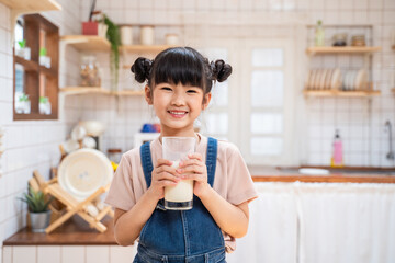 Portrait of Asian little cute kid hold cup of milk in kitchen at home.