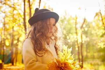 Portrait of young funny girl with blonde curly hair and in black hat in an autumn park on a yellow and orange leaf background