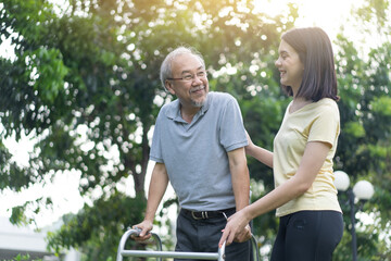 Asian young daughter help disabled senior grandfather walk in garden.