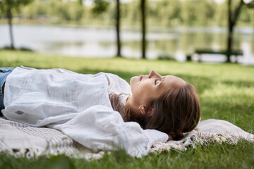 Woman relaxing in park lying with closed eyes on the blanket