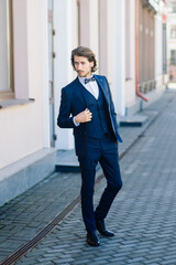 Handsome fashion businessman model dressed in elegant suit and posing on street. Metrosexual