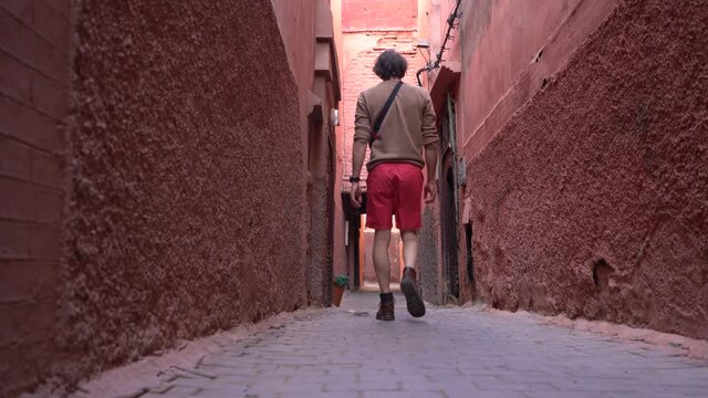 Low angle, a man walks the pink empty streets of Marrakech Medina