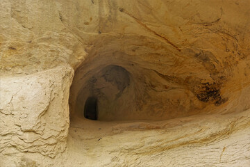 The cave was carved into the sandstone cliff of Cappadocia. Rounded vaults and a narrow dark opening in the depths. Close-up. Stone texture. Turkey