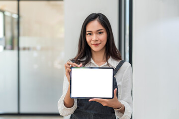 Front view of Asian businesswoman standing holding tablet blank white screen at the office. Looking at the camera.