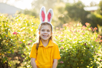 Smiling school kid outside in garden wearing rabbit ears for Easter celebrations