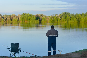 Fototapeta na wymiar Man is fishing on river with rod in early morning. Back view, selective focus, blur