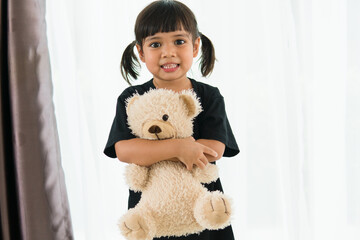 Asian girl with teddy bear is looking at the camera.
