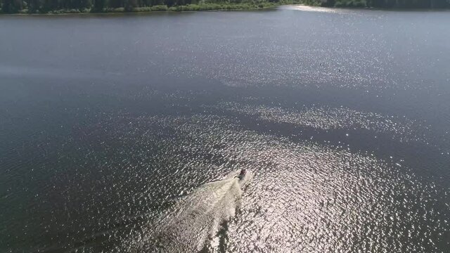 Aerial view of man ride on jetski on the city pond. The forest by the pond. Summer sunny day
