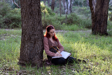 Fototapeta premium portrait of red haired girl wearing fantasy medieval clothes of a wandering adventurer. natural light in a woodland forest setting.