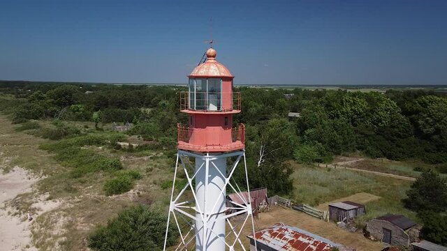 Beautiful aerial view of white painted steel lighthouse with red top located in Pape, Latvia at Baltic sea coastline in sunny summer day, wide angle drone shot orbit left