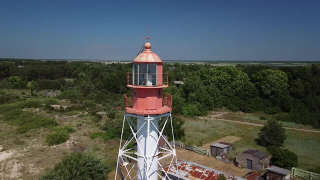 Beautiful aerial view of white painted steel lighthouse with red top located in Pape, Latvia at Baltic sea coastline in sunny summer day, wide angle drone shot orbit right