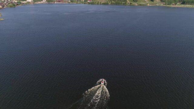 Aerial view of man ride a red and white jetski on the pond in provincial city. There are many one-story and two-story houses, church, forest and mountain on the Shore. Summer sunny day
