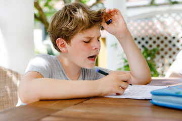 Hard-working sad school kid boy making homework during quarantine time from corona pandemic disease. Upset tired child on home schooling in coronavirus covid time, schools closed.