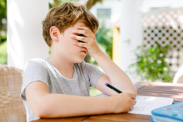 Hard-working sad school kid boy making homework during quarantine time from corona pandemic disease. Upset tired child on home schooling in coronavirus covid time, schools closed.