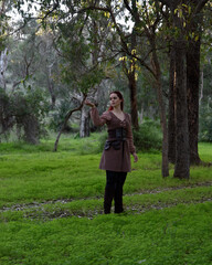 Fototapeta premium portrait of red haired girl wearing fantasy medieval clothes of a wandering adventurer. natural light in a woodland forest setting.