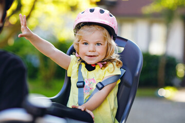 Portrait of little toddler girl with security helmet on the head sitting in bike seat of parents....
