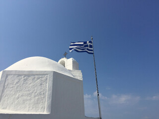 The Greek National Flag flies next to the Church Saint Nicholas the Thalassinos, a Greek Orthodox Church located on the pier at the entrance to the Aegina Marina on Aegina Island, Greece