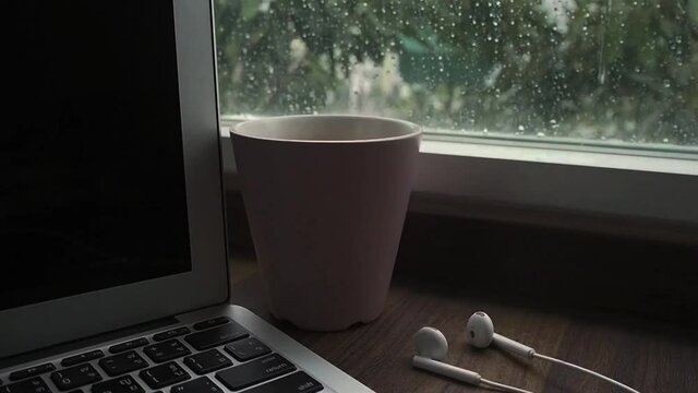 computer notebook next to a cup coffee on rainy day window background