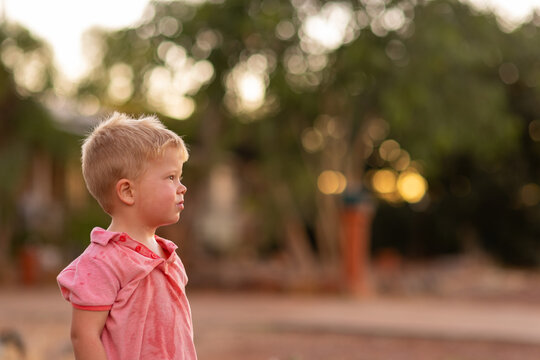little blonde-haired boy with dishevelled shirt offset with blurry background