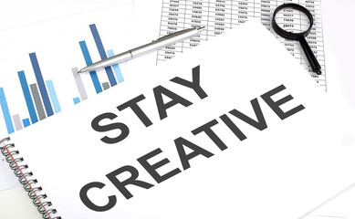 In the notebook, the text STAY CREATIVE , next to magnifier and a pen, the background is graphics.