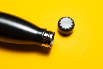 Close-up of opened, reusable steel thermo water bottle and cap on yellow background.