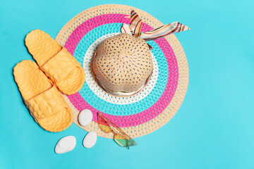 Top view of woman summer hat with yellow slippers near sunglasses and stones on blue background.