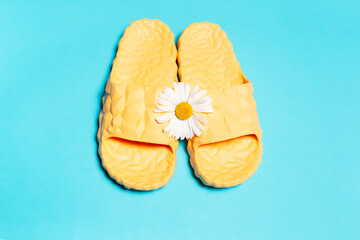 Top view of yellow slippers and chamomile flower on blue background.