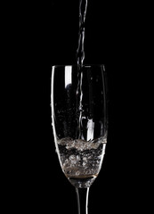 Pouring water from bottle into glass on black background
