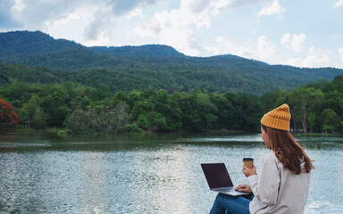 A young woman using and working on laptop computer while traveling mountains and lake