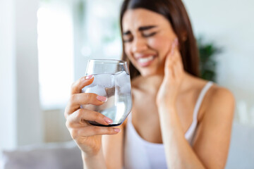 Young woman with sensitive teeth and hand holding glass of cold water with ice. Healthcare concept. woman drinking cold drink, glass full of ice cubes and feels toothache, pain