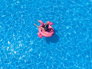 woman swimming with pink flamnigo in pool from above view, aerial top view from drone, summer relaxation in hotel