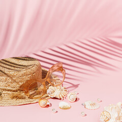 Beach straw hat and feminine eyeglasses under a shadow of palm leaf with seashells and snails on pastel pink background. Creative sea travel concept. Minimal tropical beach and vacation idea.