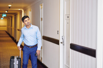 Fototapeta na wymiar Mature man searching for his room , he is walking down corridor and pulling suitcase