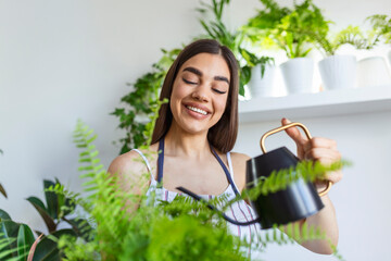 Joyful young woman enjoys her time at home and watering her plant by the window at home. woman...