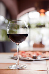 Wine glass filled with red wine on a wooden table with blurred background in restaurant.