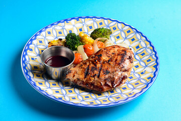 Delicious grilled beef steak with bbq vegetables and corn served on a white plate with sauce over blue background.