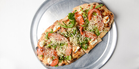 Pinza with vegetables and meat cooked in an oven with wood and served on a metal tray over white background.